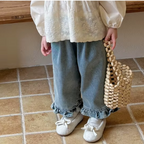 Person wearing a white blouse, blue jeans, and white shoes, holding a woven bag on a tiled floor.
